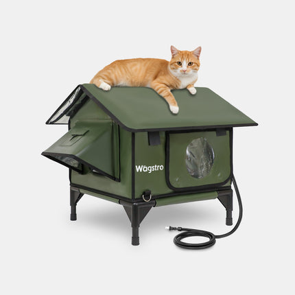 An orange and white cat lies on top of a green Wagstro elevated cat house with a small window and open front panel, photographed on a light gray studio background.